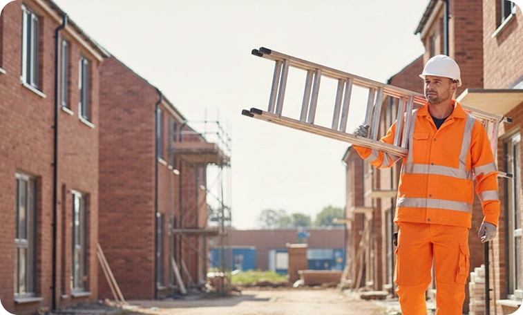 Tradesperson carrying an aluminium ladder on a building site