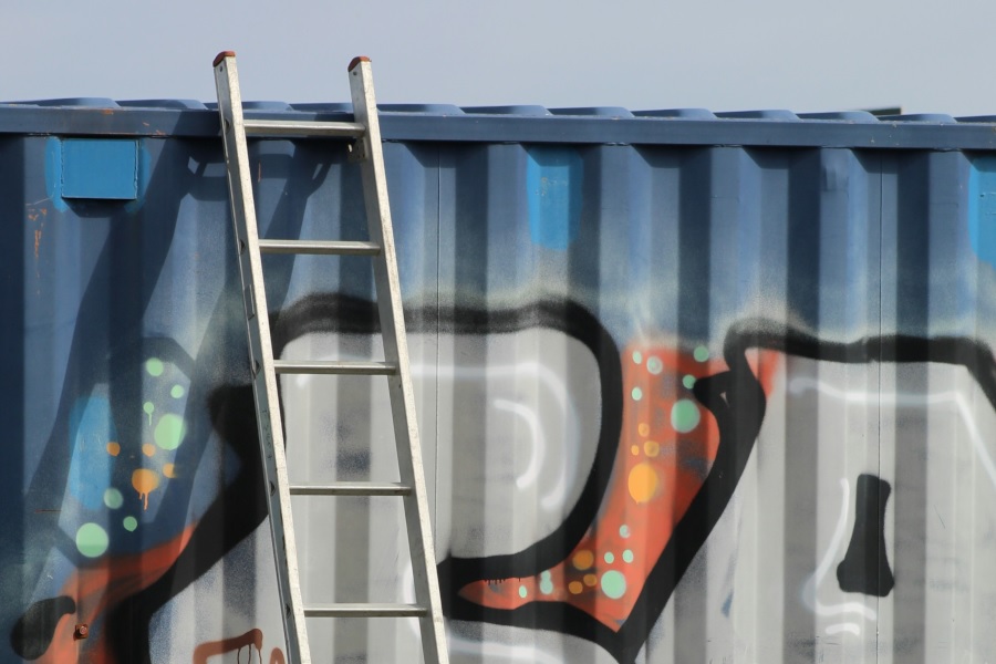 aluminium ladder leaning up against shipping container decorated with graffiti - Do Ladders Have Expiration Dates?