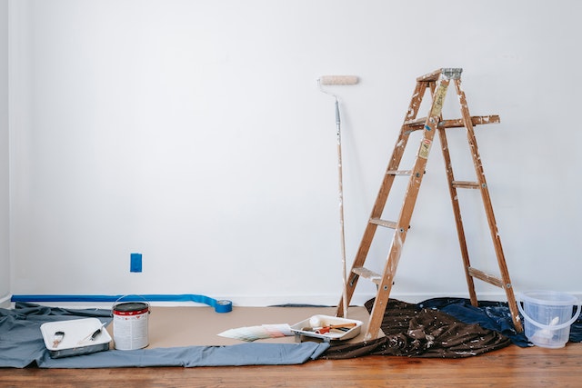 wooden step ladder propped infront of white wall with paint sheets and paintbrushes on the floor