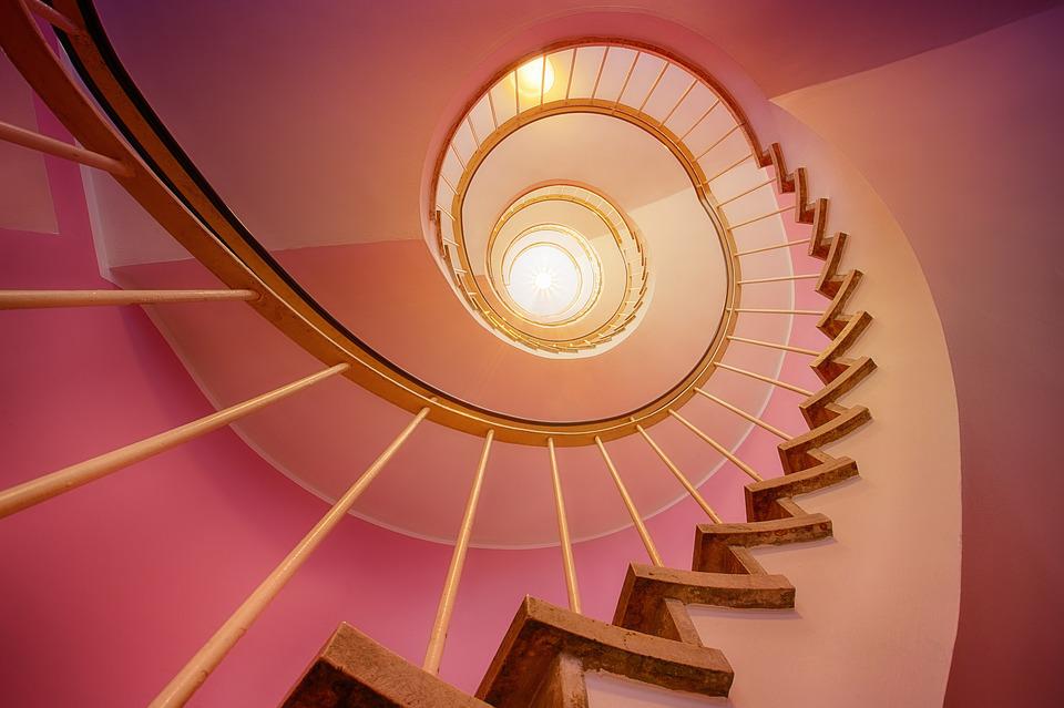 low angle shot of pink spiral stairs, illuminated by a skylight at the top of the stairs 
