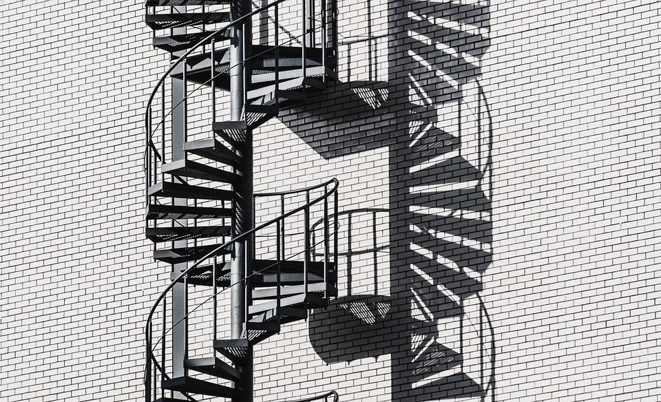 modern and minimalist black external spiral stairs infront of light grey brick wall